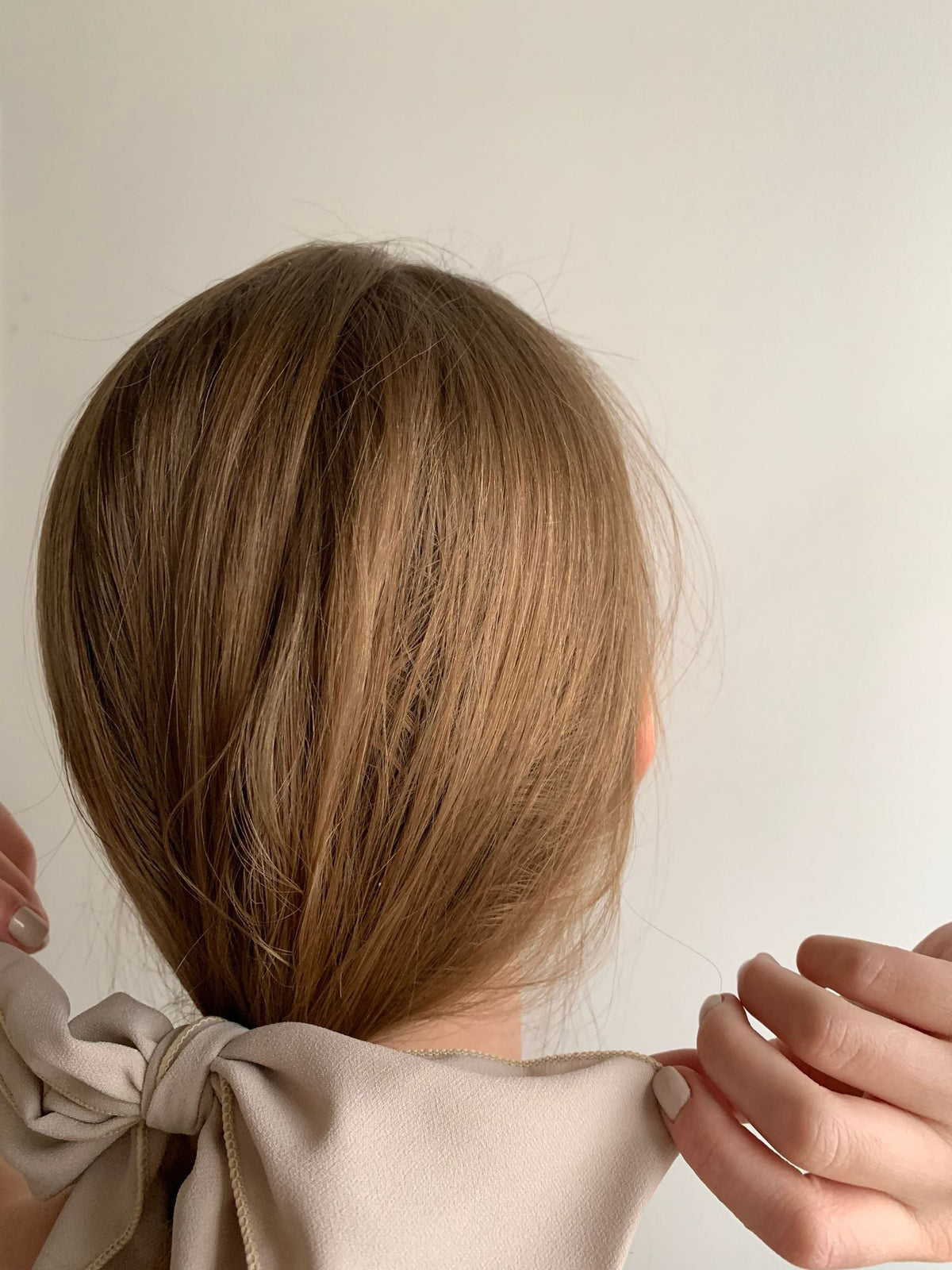 Femme blonde de dos nouant un ruban en nœud dans ses cheveux, coiffure avec foulard aux tons beige Image