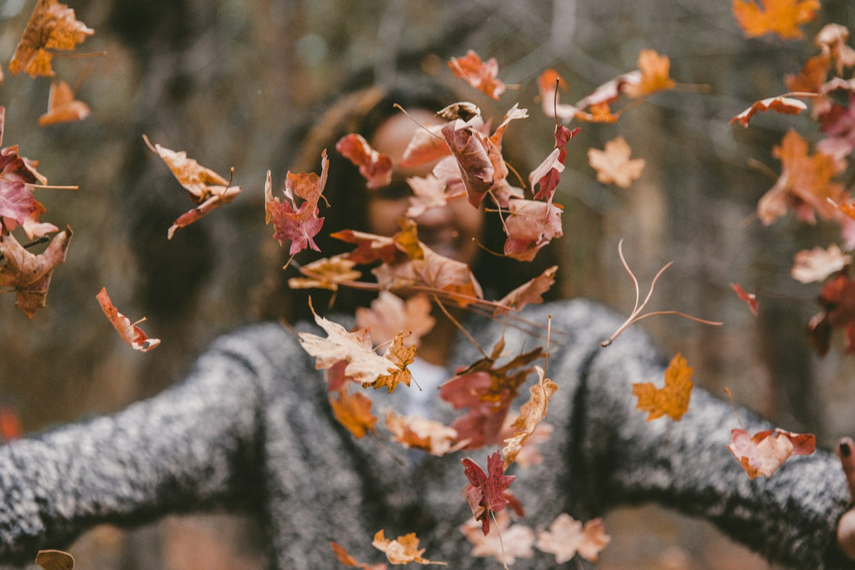 Femme souriante lançant des feuilles d'érable dorées en automne, cheveux au vent