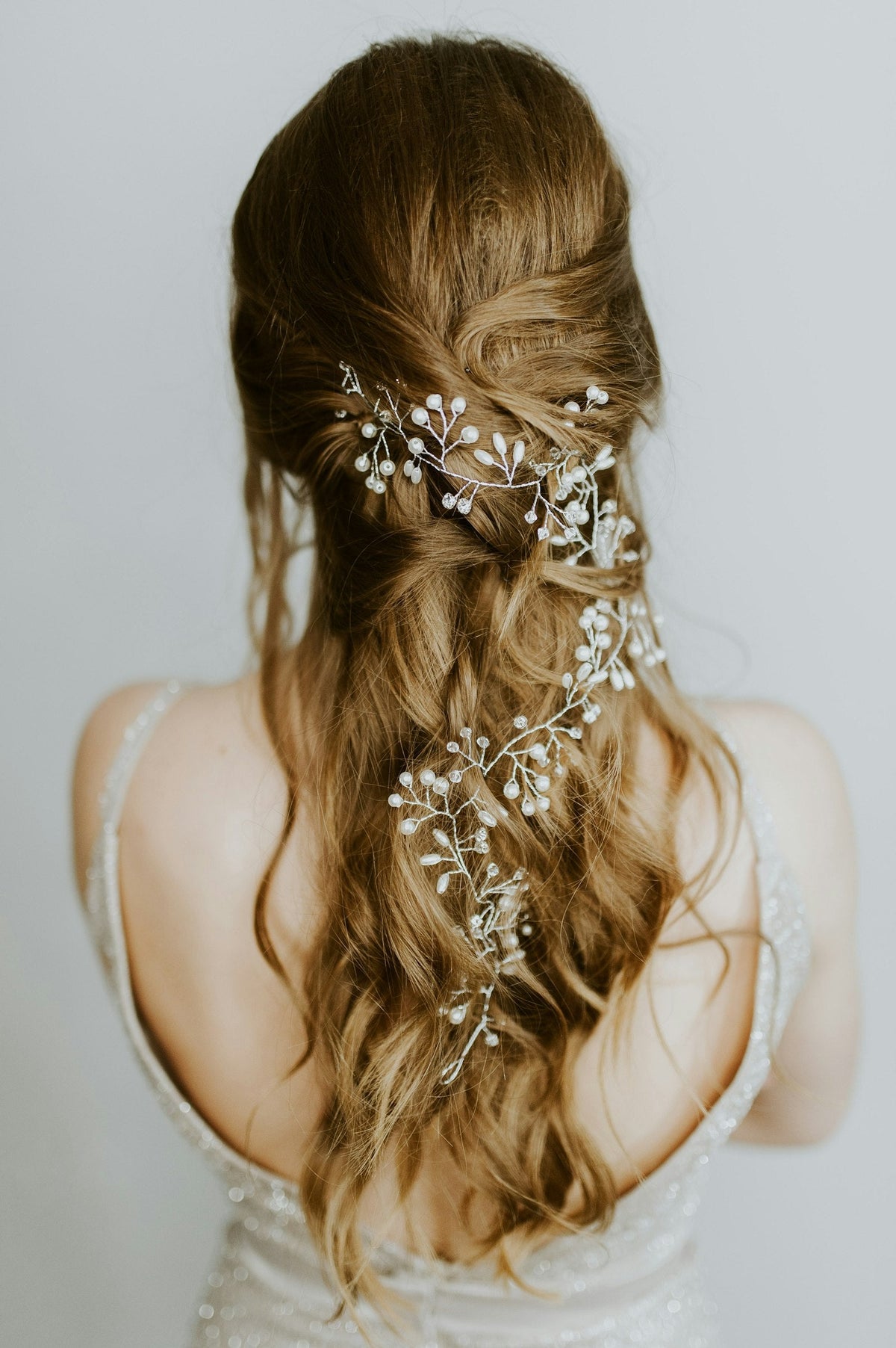 Femme aux cheveux bruns relevés en coiffure romantique, ornée d'un accessoire floral blanc pour un mariage