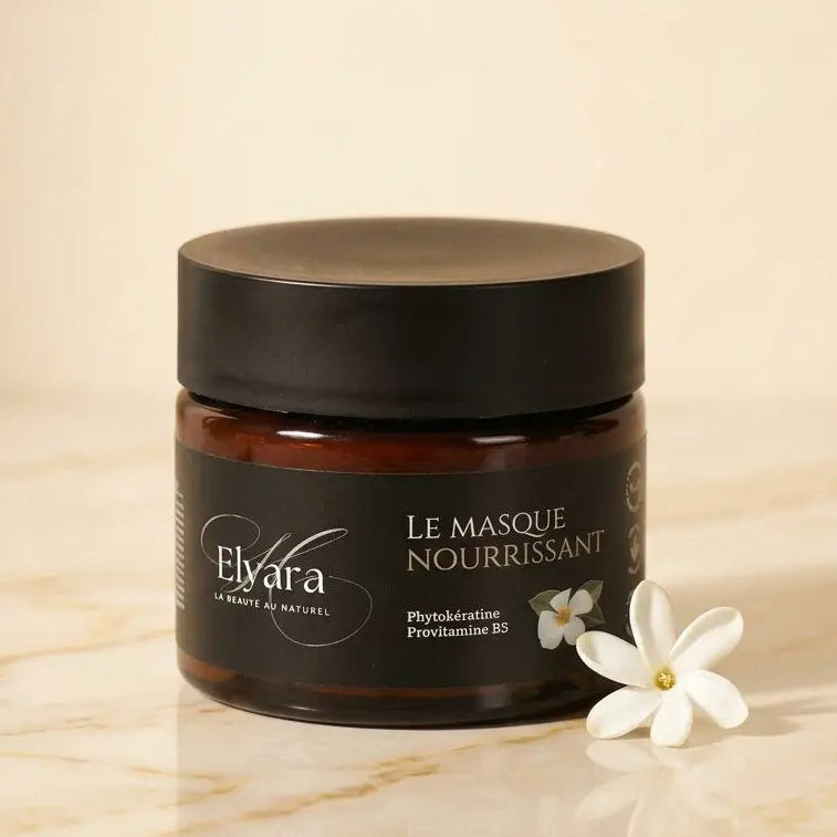 Pot de masque nourrissant pour cheveux secs et endommagés (Elvara) avec fleur blanche à côté.