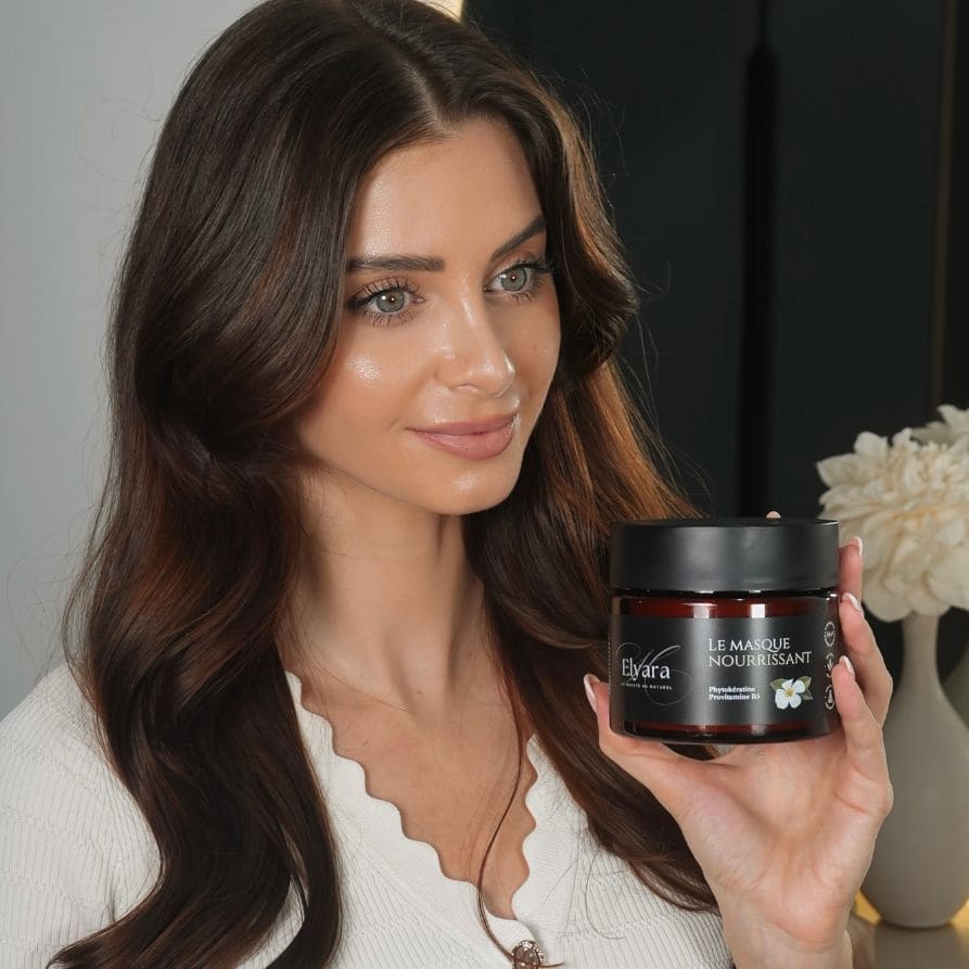 Femme tenant un pot rouge sombre de masque nourrissant pour cheveux secs et abîmés, label Le Masque Nourrissant, noir et blanc.